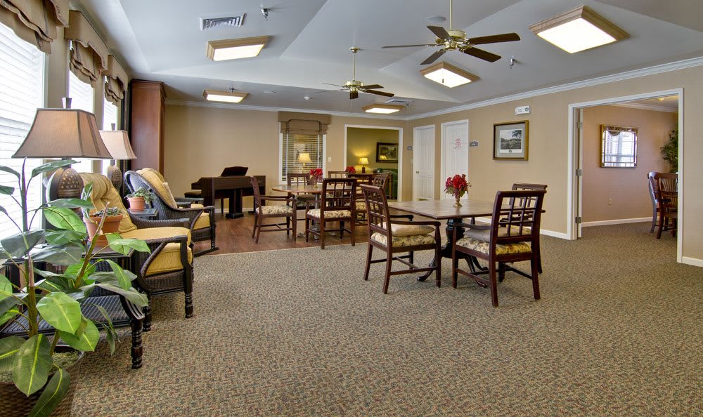 A spacious and comfortable lounge area with tables, chairs, ceiling fans, and a piano.