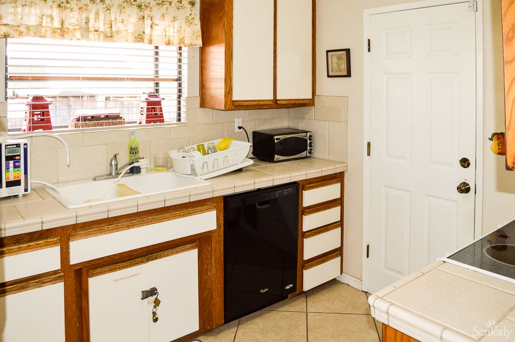 A cozy kitchen interior featuring a sink, microwave, dish rack, and wooden cabinets.