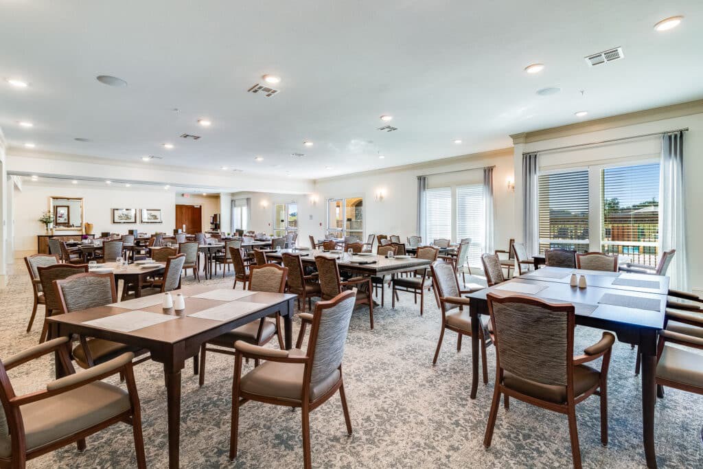 Spacious dining area with multiple tables and chairs, featuring large windows and soft lighting.