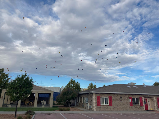 A picturesque view of the sky filled with balloons, contrasting against the clouds and surrounding buildings.