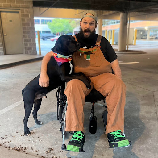 A man in a wheelchair enjoys the company of his dog in an urban environment.