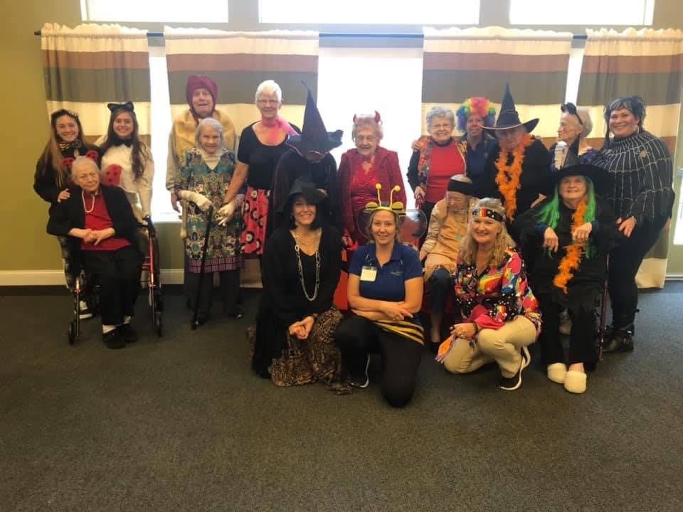 A group of people dressed in festive Halloween costumes, including several witch outfits, gathered together indoors.