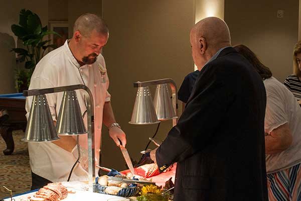A chef is carving meat at a buffet station while guests are being served.