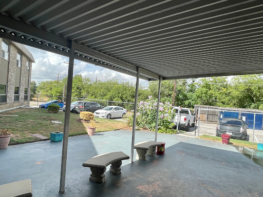 A covered outdoor patio area with benches, overlooking a parking space and greenery.