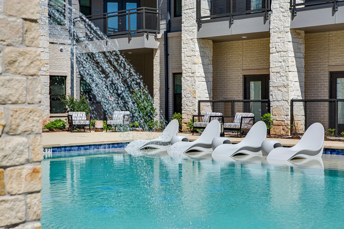 A serene outdoor pool area featuring a waterfall and comfortable lounge chairs.