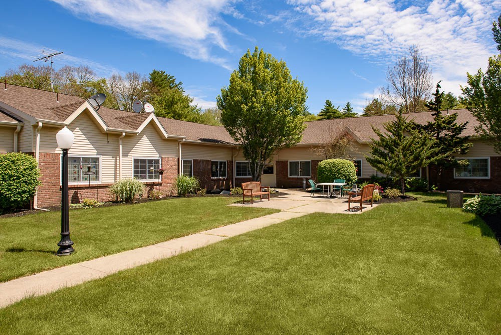 A cozy house with a spacious lawn and outdoor seating under a partly cloudy sky.
