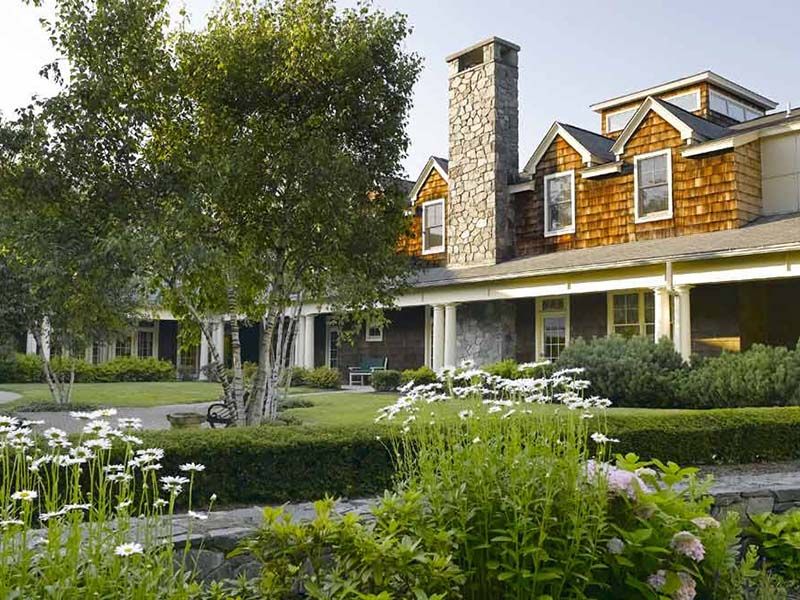 A beautiful house with a lush garden and stone chimney, surrounded by greenery.