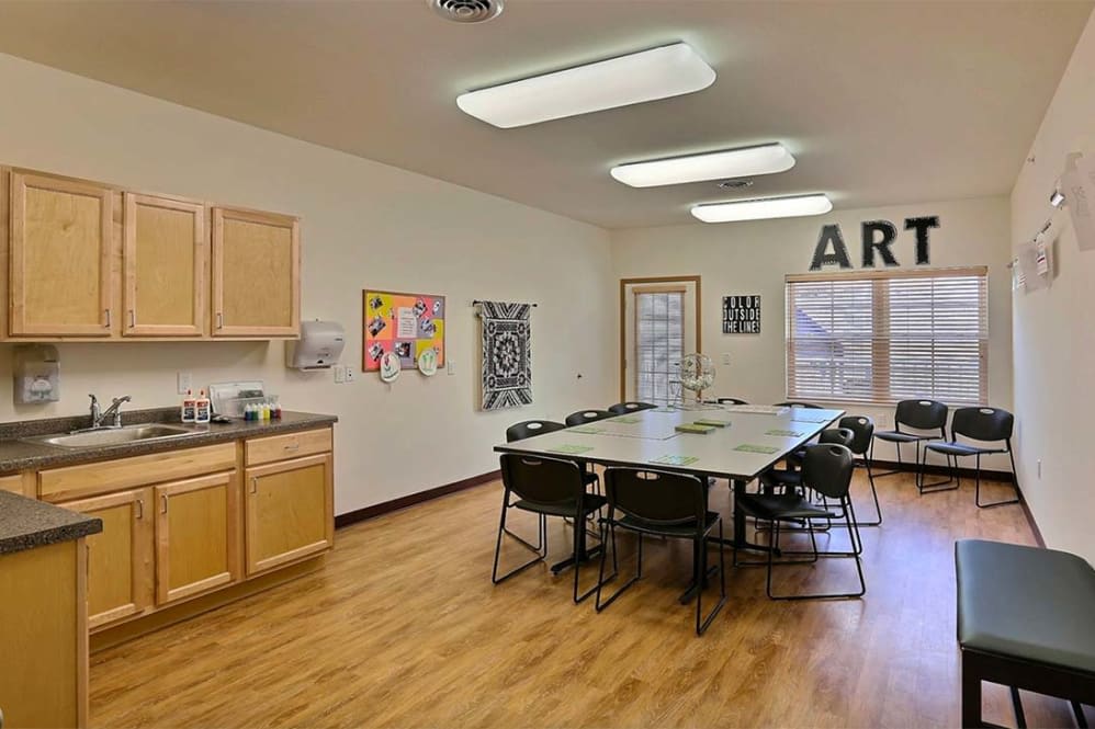 An art classroom with a large table surrounded by chairs, showcasing artwork on the walls.