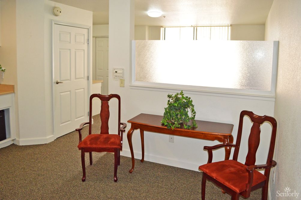 A cozy waiting area with two red upholstered chairs, a wooden table, and a potted plant under soft lighting.