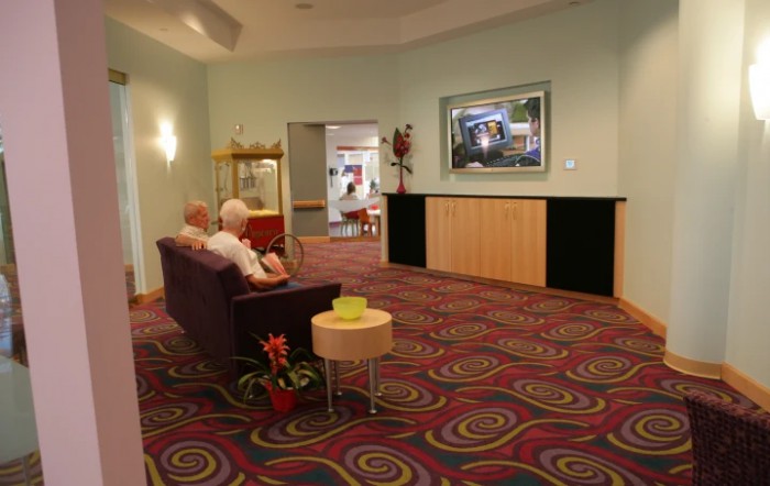 A cozy lobby with vibrant carpet, a couch, and a television on the wall.