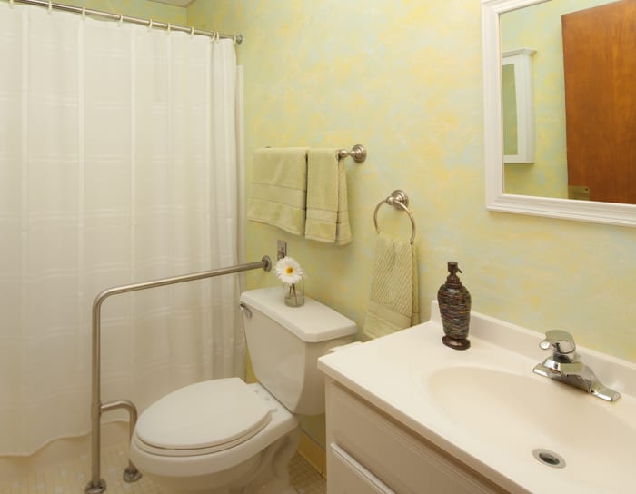 A clean and simple bathroom with a toilet, sink, mirror, and shower.