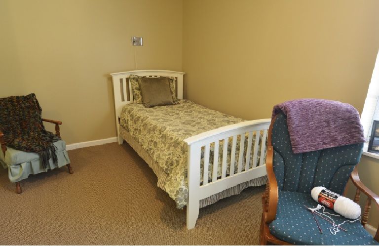 A cozy bedroom featuring a single bed with patterned bedding and an upholstered chair in the corner.