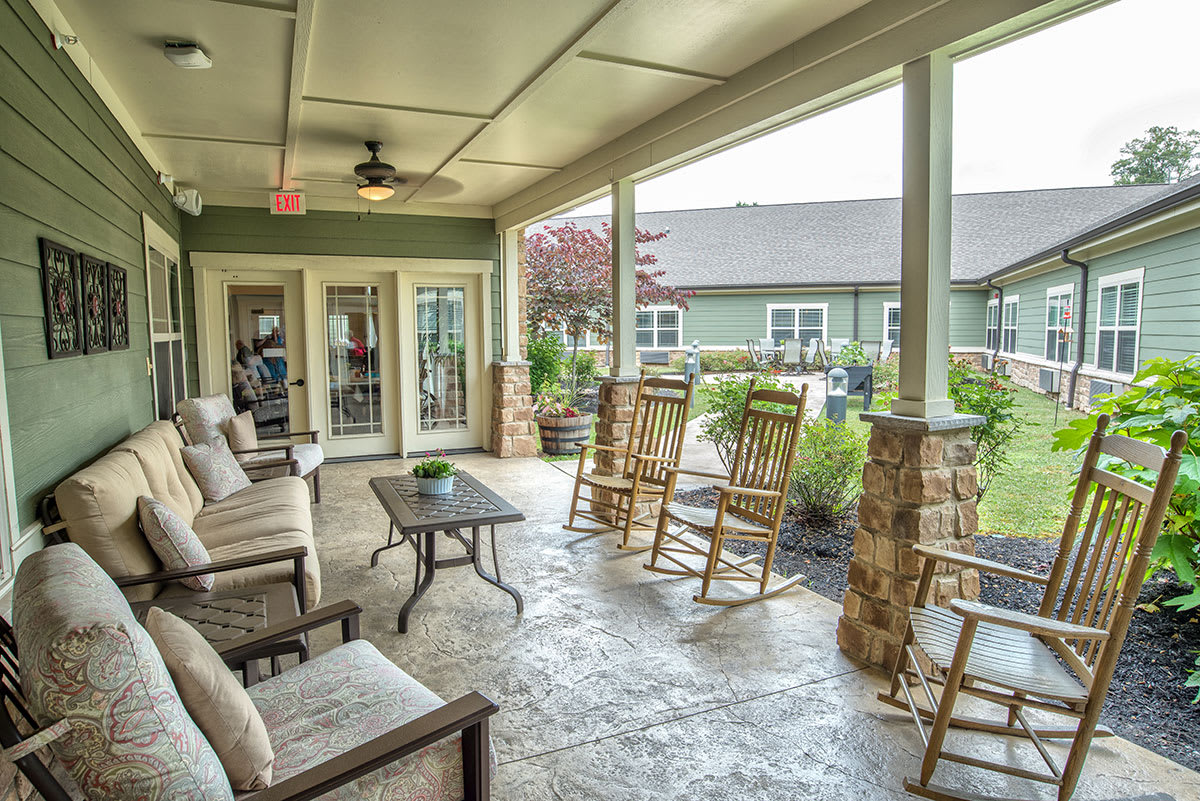 A cozy covered porch with rocking chairs and outdoor seating, surrounded by plants.