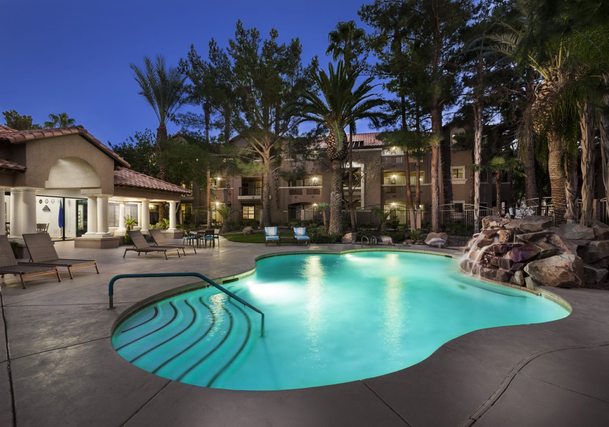 A serene outdoor pool area illuminated at night with palm trees in the background.