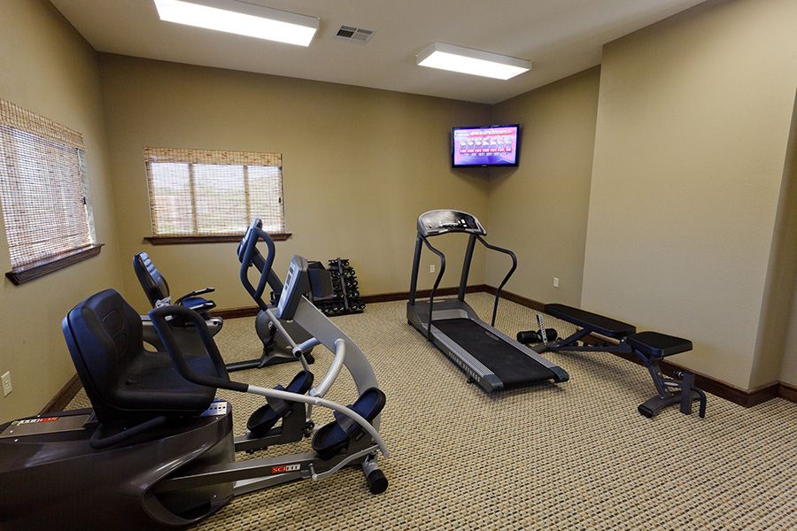 A small gym featuring a treadmill, exercise bikes, and a wall-mounted TV.