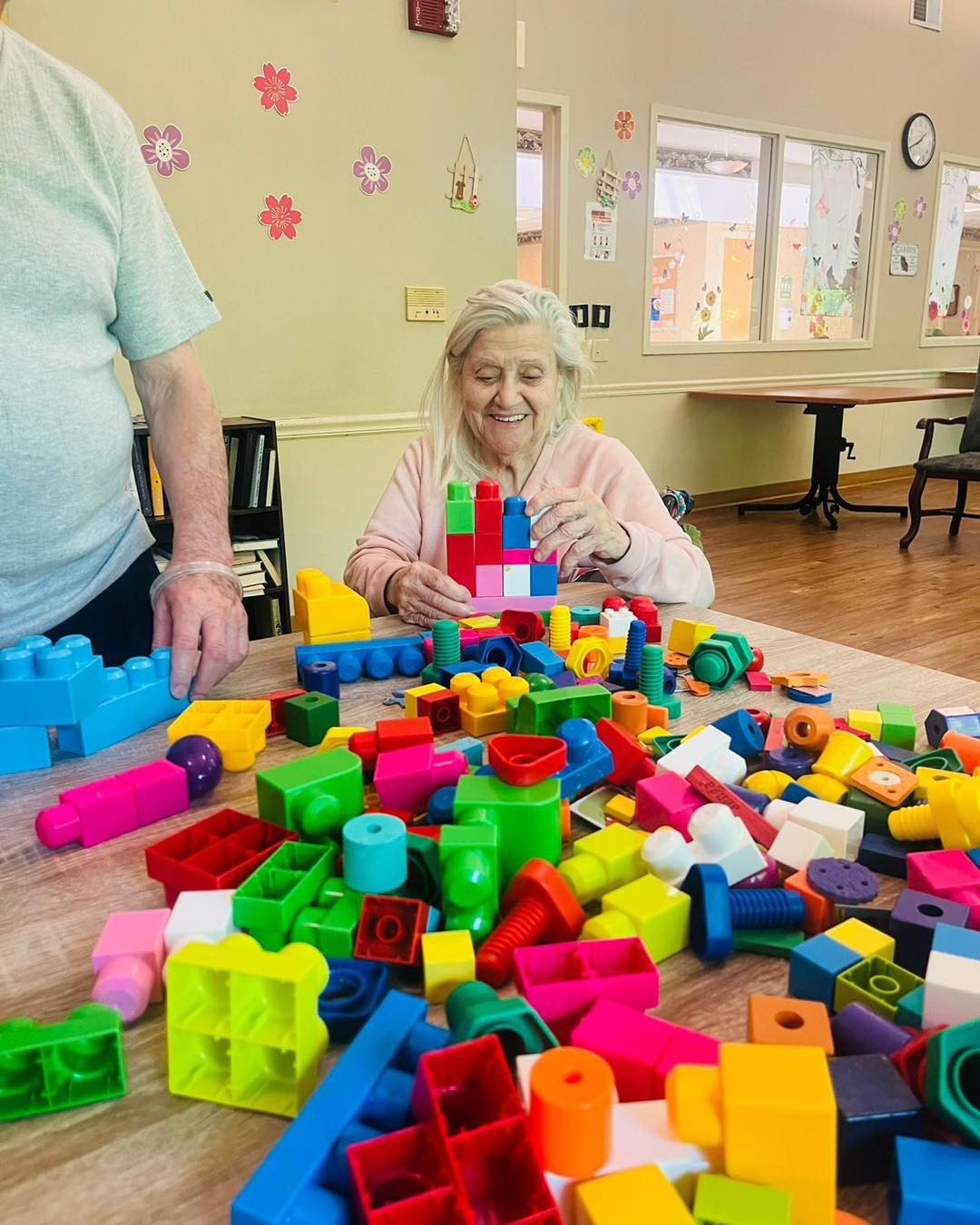 An elderly woman enjoying building with colorful blocks in a community center.