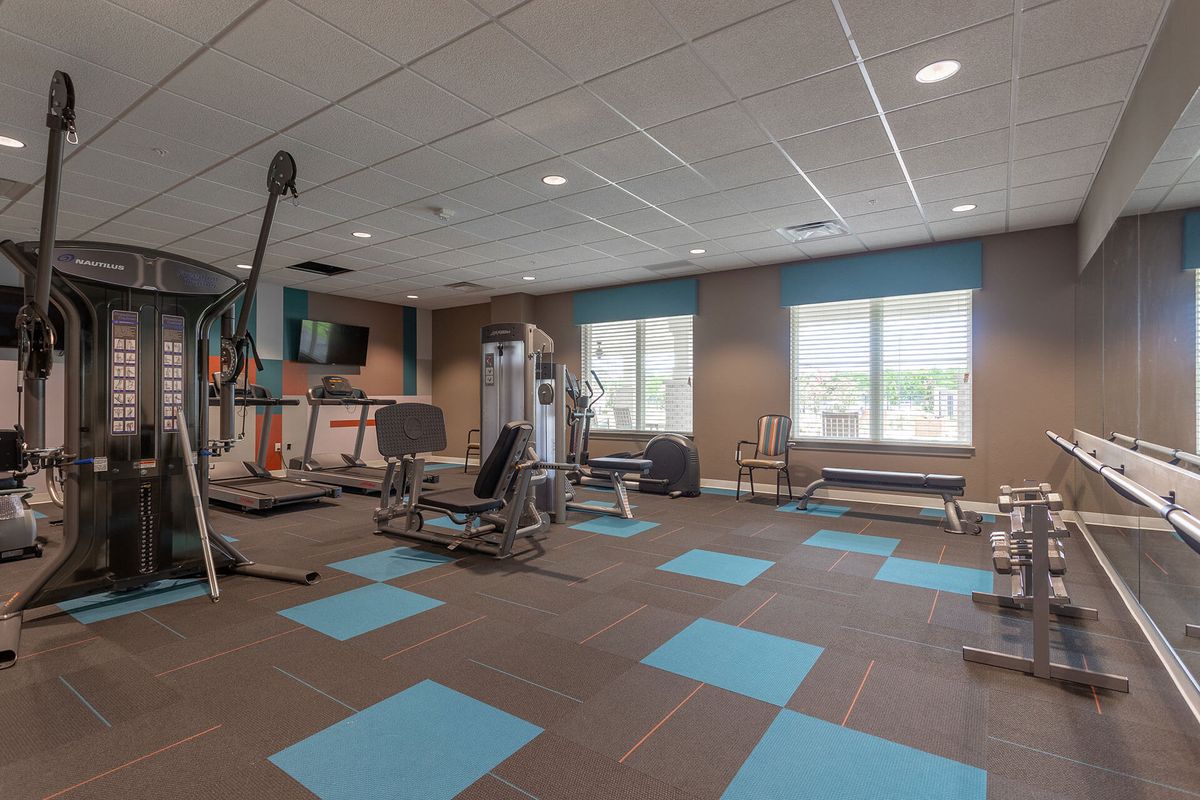A well-equipped gym with exercise machines, weights, and large windows providing natural light.