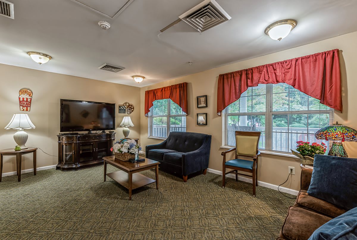 A cozy living room with a television, couch, coffee table, and large windows adorned with red curtains.