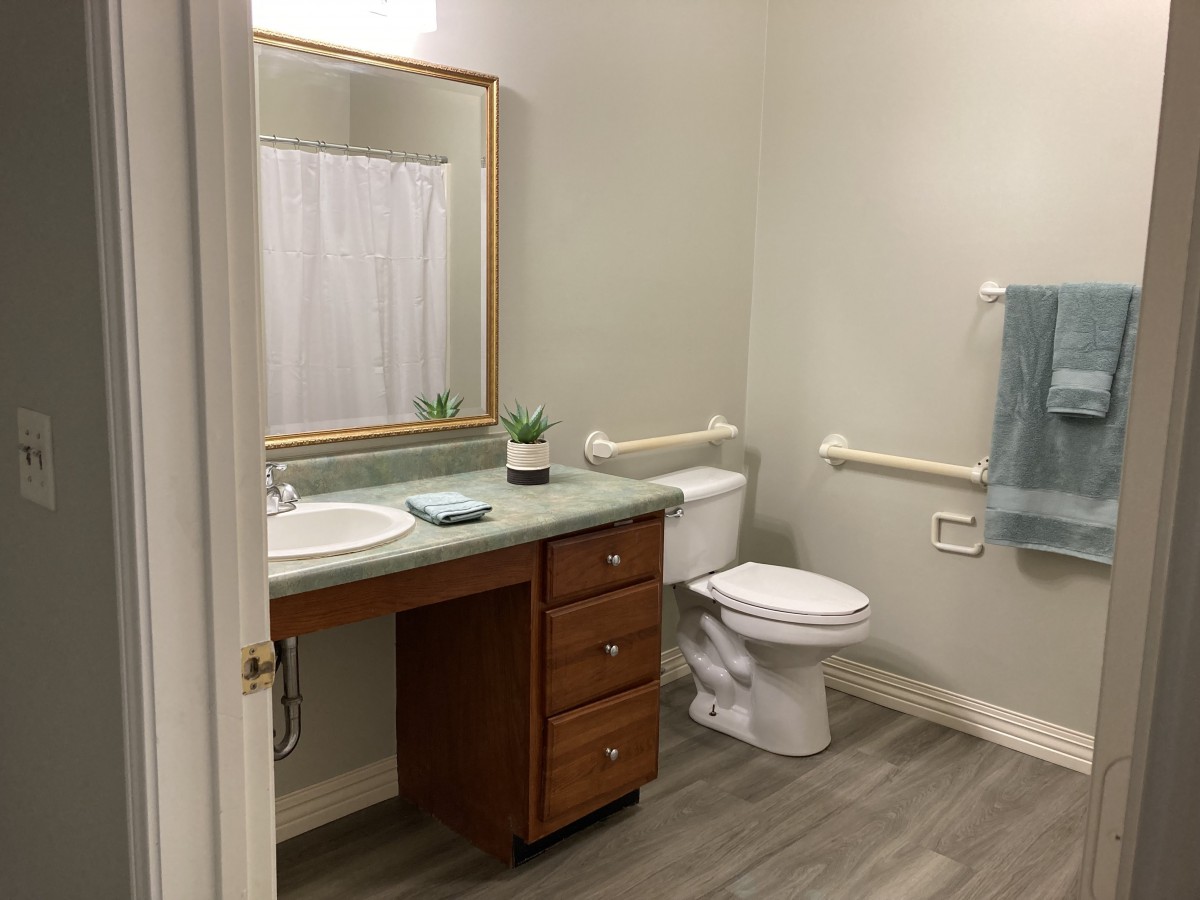 A clean and simple bathroom with a sink, mirror, and toilet, featuring wooden cabinetry and light-colored walls.