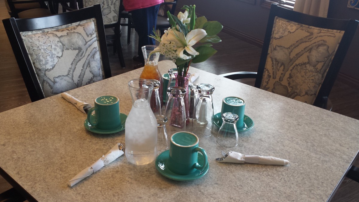A neatly arranged dining table with cups, a vase of flowers, and cutlery.