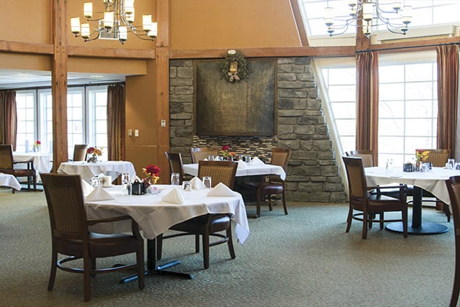 A cozy restaurant dining area with neatly set tables and chairs, featuring a stone accent wall and large windows.