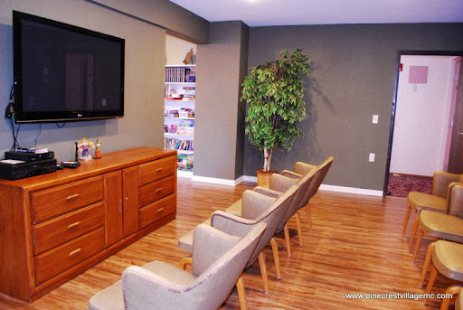 A cozy waiting area featuring comfortable chairs, a wooden cabinet, and a television, complemented by a decorative plant.