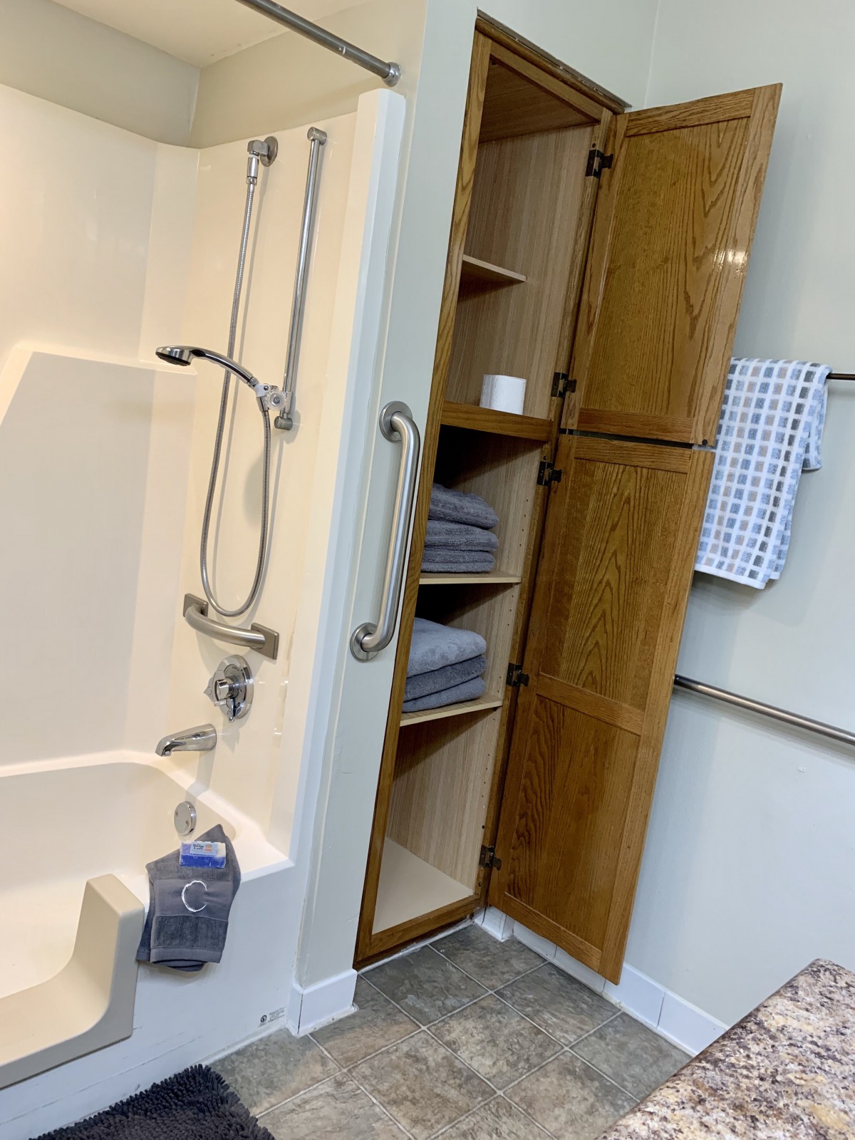 An accessible bathroom with a shower and storage cabinet, featuring grab bars for safety.