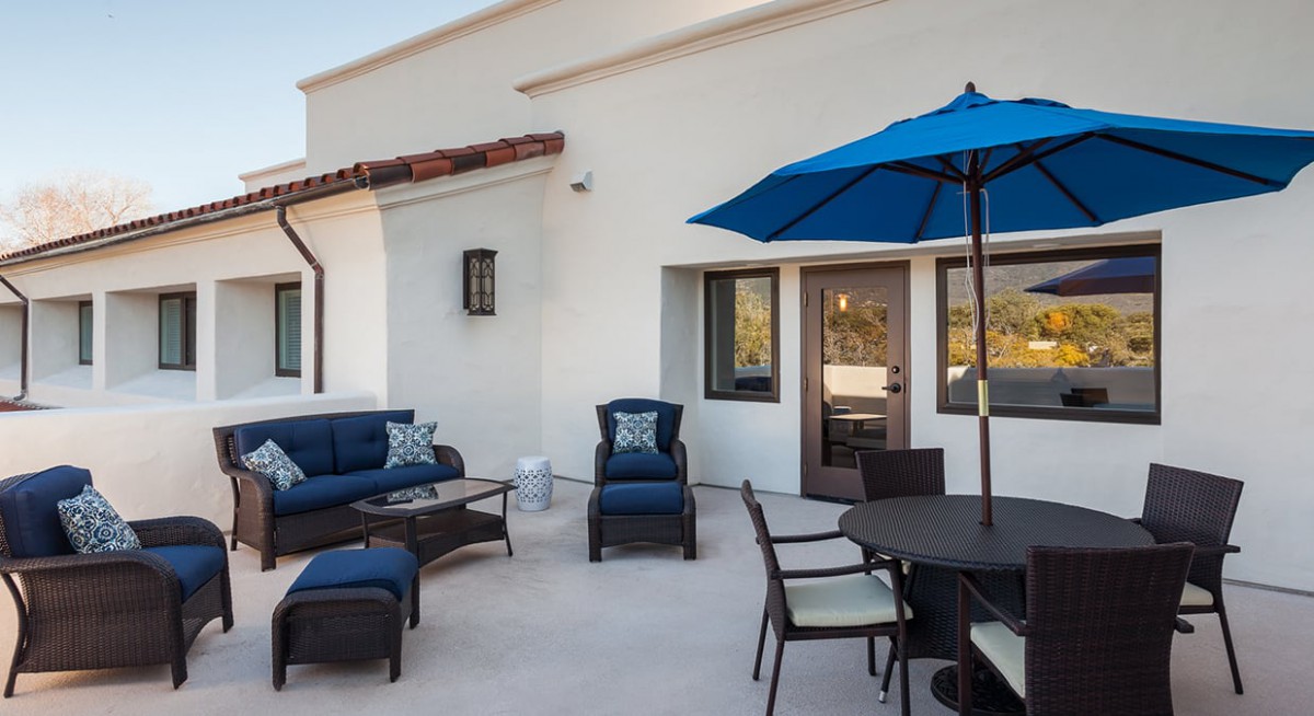 A modern patio with comfortable outdoor seating, a blue umbrella, and stylish furniture.