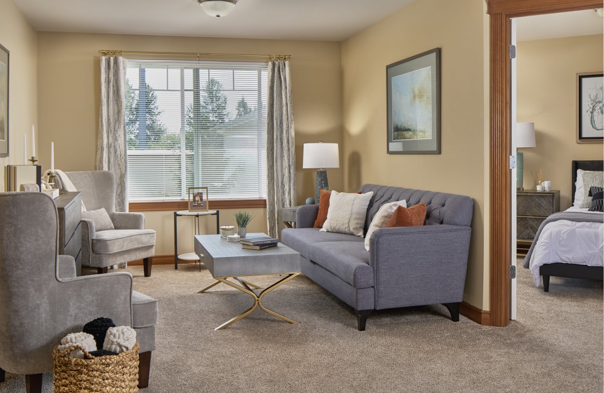 A cozy living room featuring a sofa, armchair, and coffee table with a large window letting in natural light.