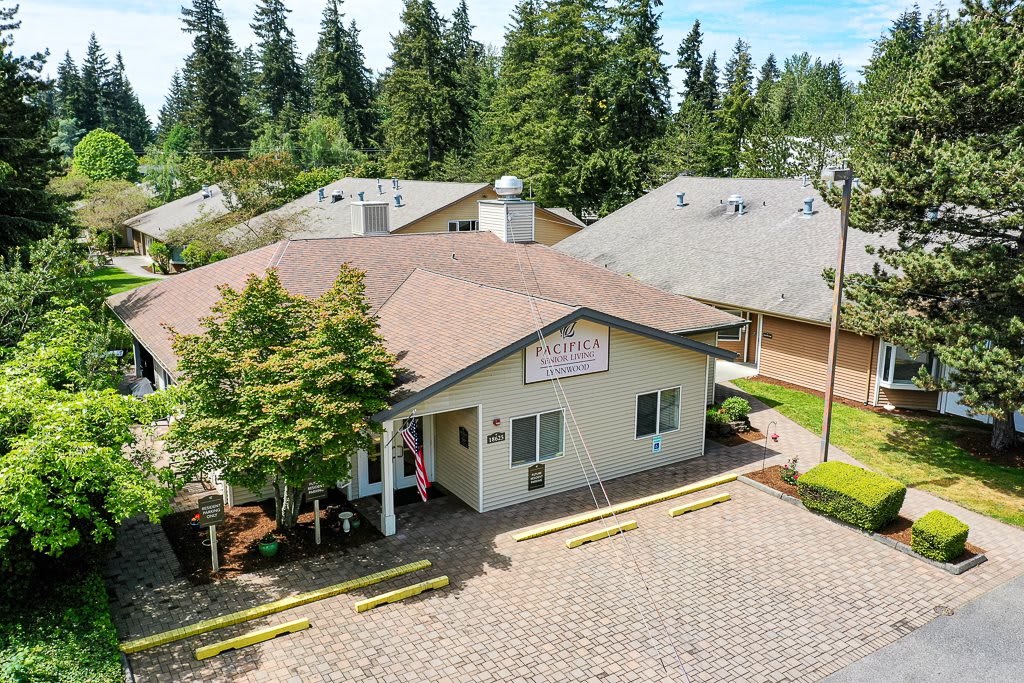 Aerial view of a small building surrounded by trees and adjacent to a paved driveway.