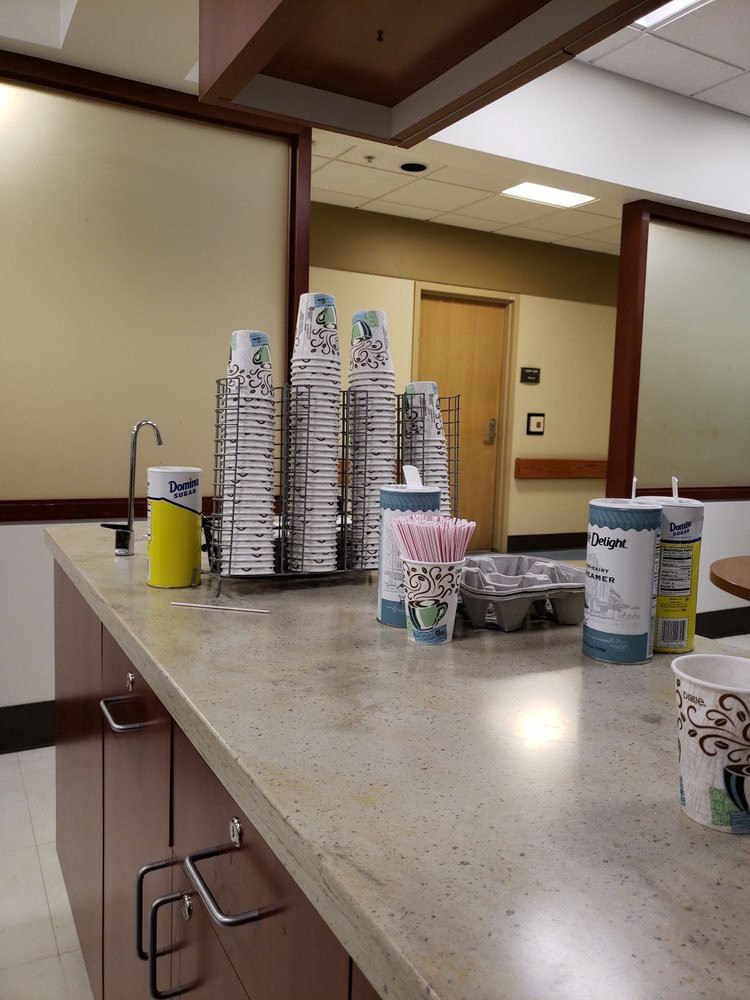 A coffee station in a clinic waiting area with stacks of paper cups arranged on a countertop.