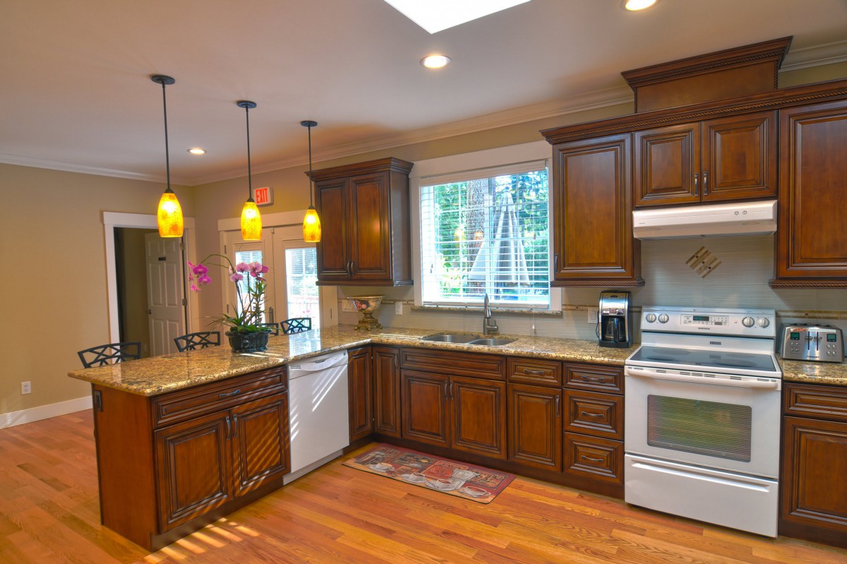 A spacious kitchen featuring wooden cabinets, granite countertops, and modern appliances, illuminated by pendant lights and natural light from a skylight.