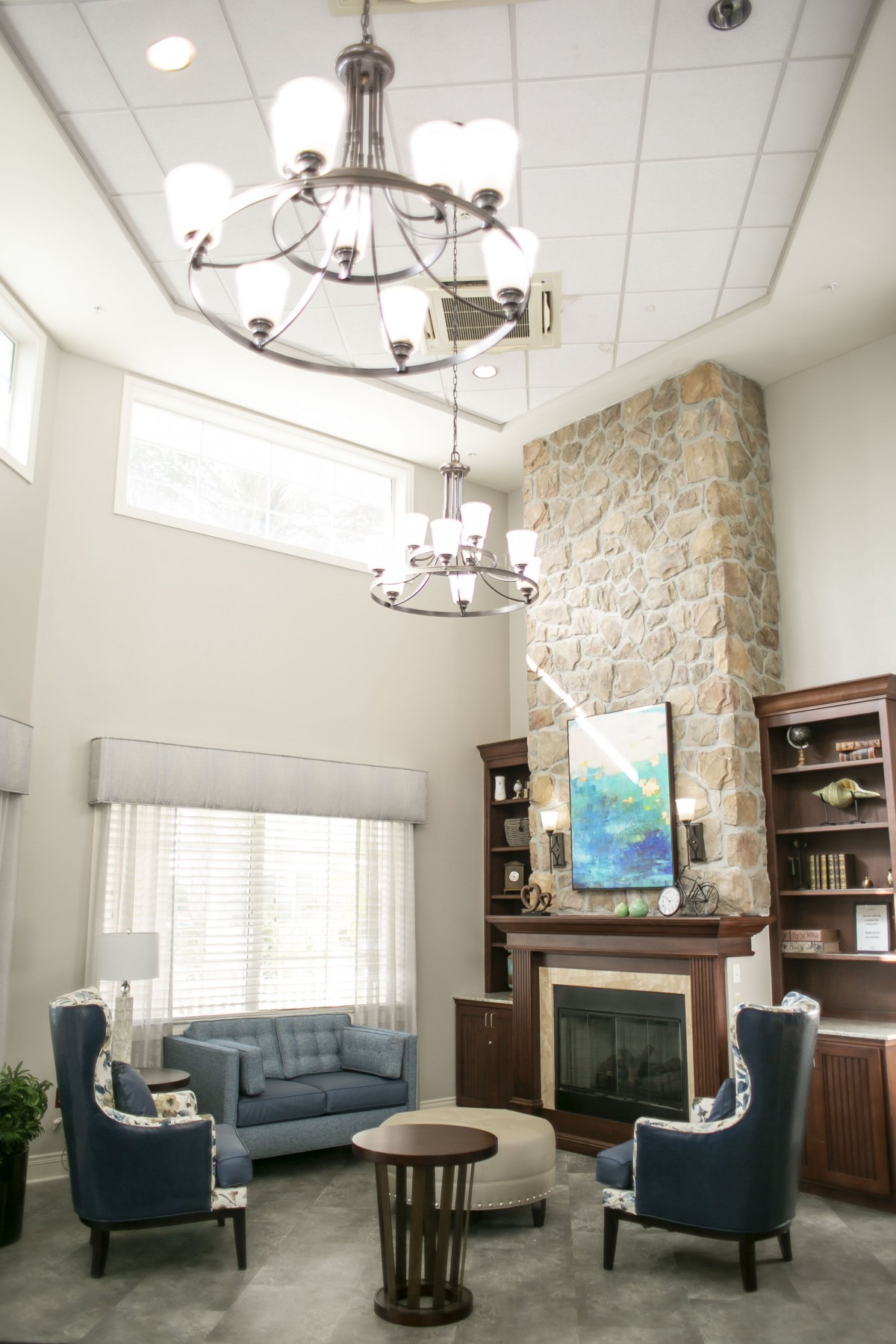 A spacious living room with a vaulted ceiling, featuring a stone fireplace, elegant chandelier, and ample natural light.