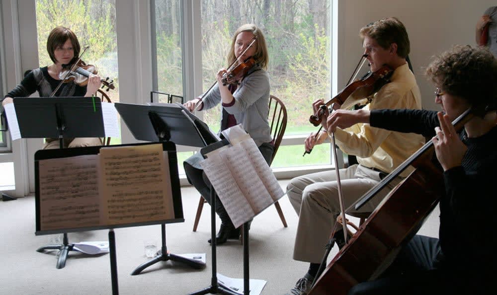 A string quartet rehearses with music sheets in a well-lit room.