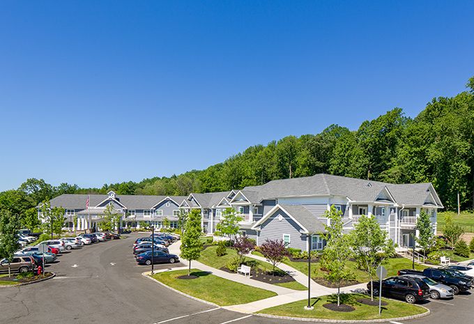 A view of a suburban apartment complex with well-maintained landscaping and ample parking under a clear blue sky.