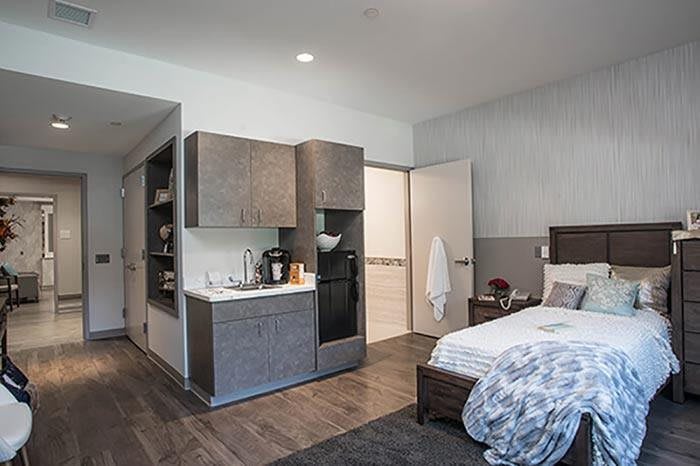 A modern apartment bedroom with a kitchenette and minimalist decor.