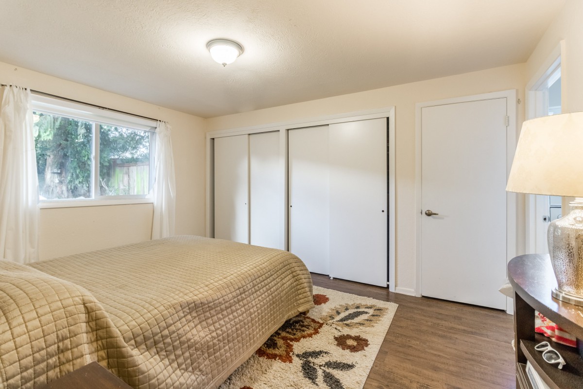 A minimalist bedroom featuring a bed with a quilt, three closets, and a window letting in natural light.