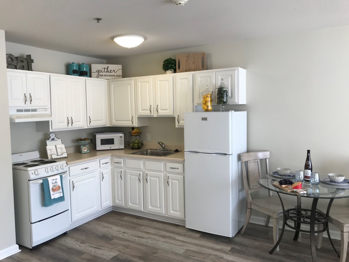 A modern kitchen with white cabinets, appliances, and a small dining area.