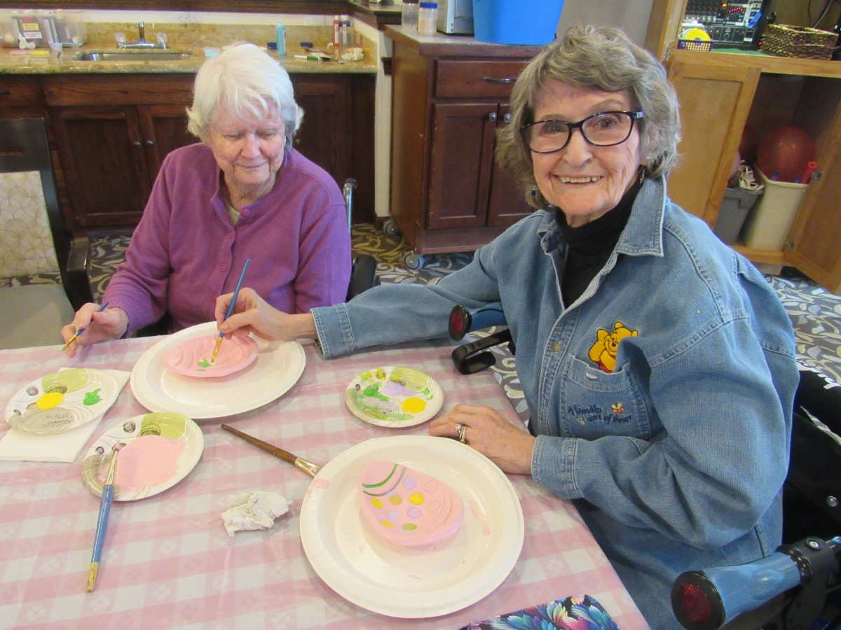 Two elderly women enjoying a painting craft activity indoors.