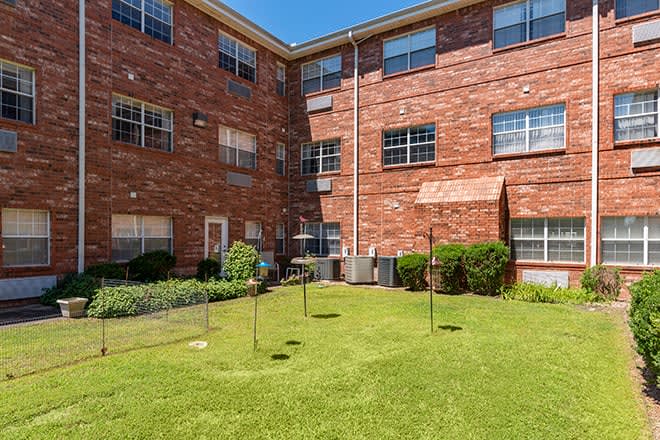 A sunny courtyard of a brick apartment building with a well-maintained lawn.