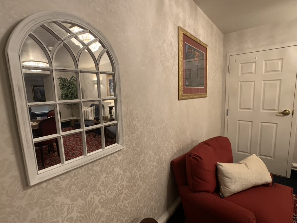 A cozy living room with a red sofa, decorative pillows, and an arch mirror reflecting the room's interior.