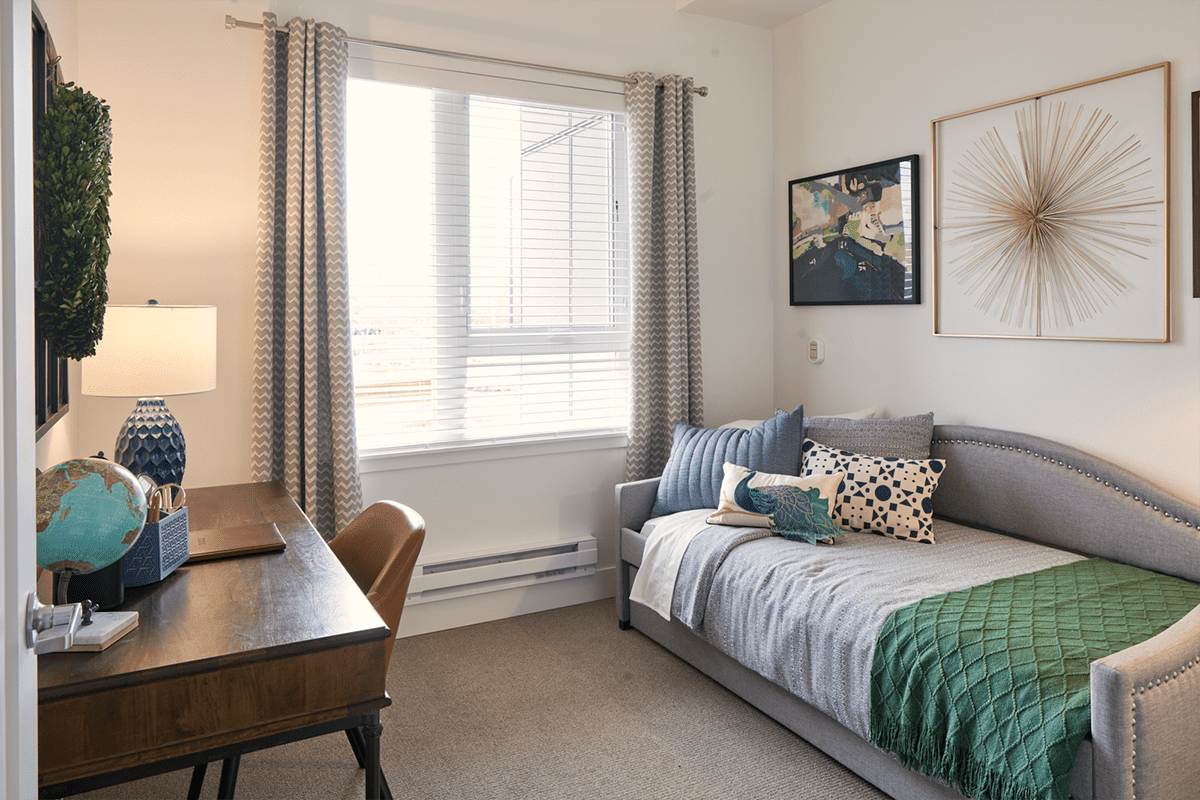 A cozy bedroom with a daybed, desk, and window adorned with curtains.