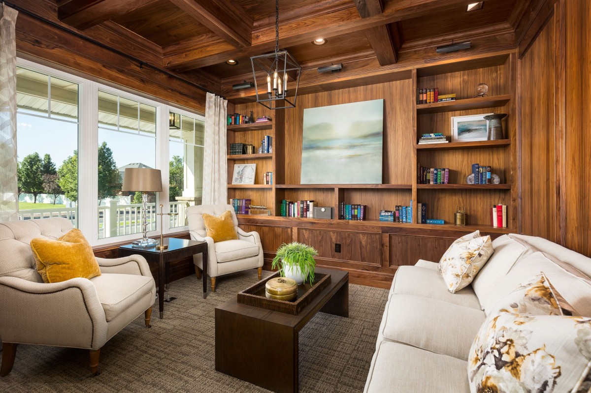 A beautifully designed living room with wooden paneling, coffered ceiling, and ample natural light highlighting modern furniture and built-in bookshelves.