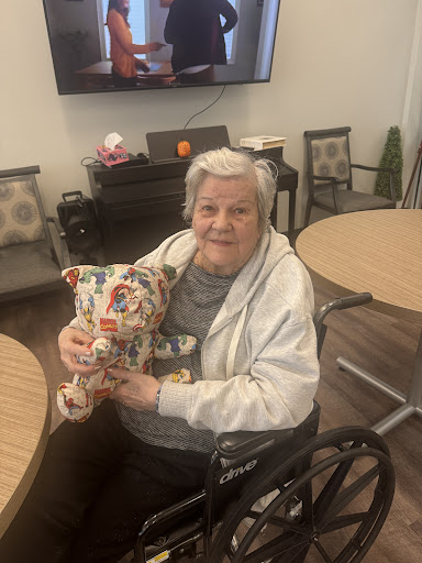 An elderly woman in a wheelchair joyfully holding a colorful stuffed animal in a care facility.