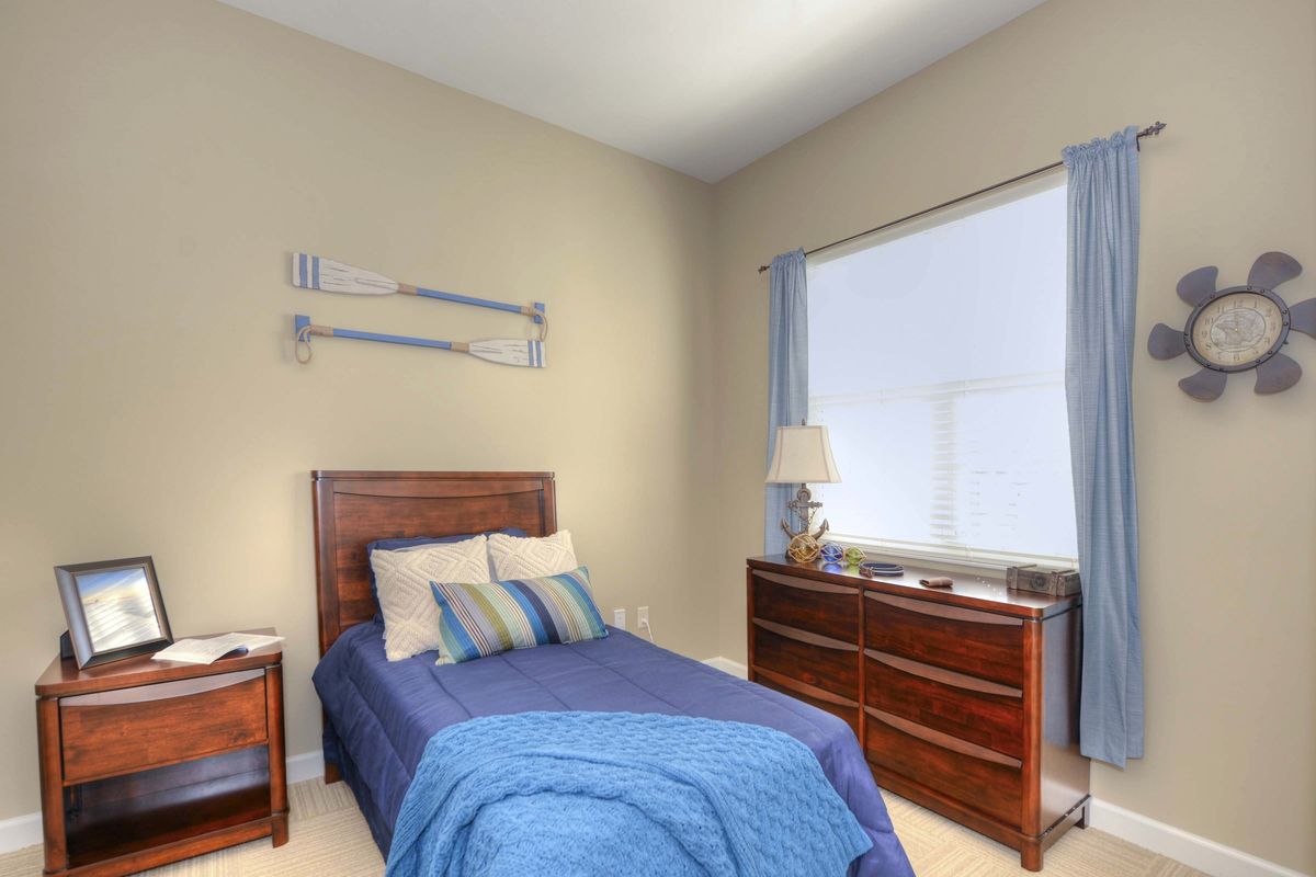 A cozy bedroom with a single bed featuring blue bedding, a wooden dresser, and a window with curtains.