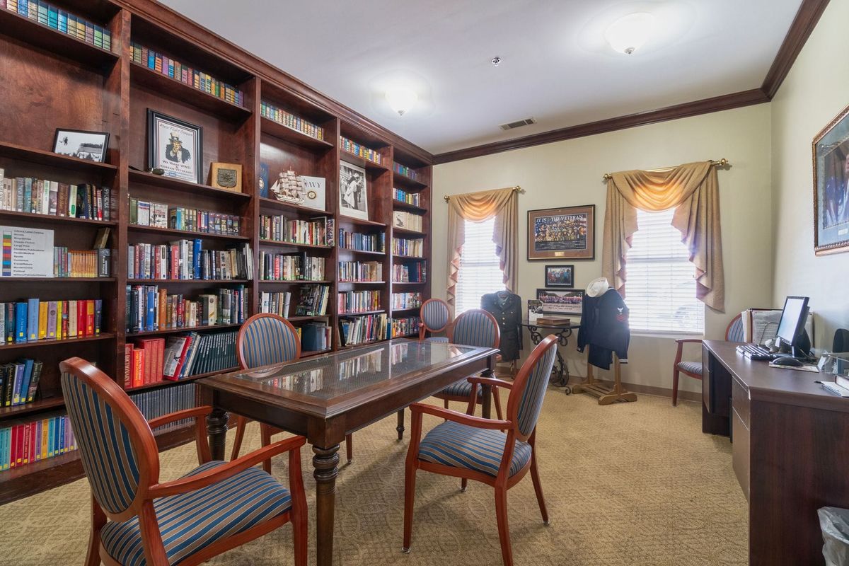 A cozy library room with bookshelves filled with books, a wooden table, and chairs for reading.