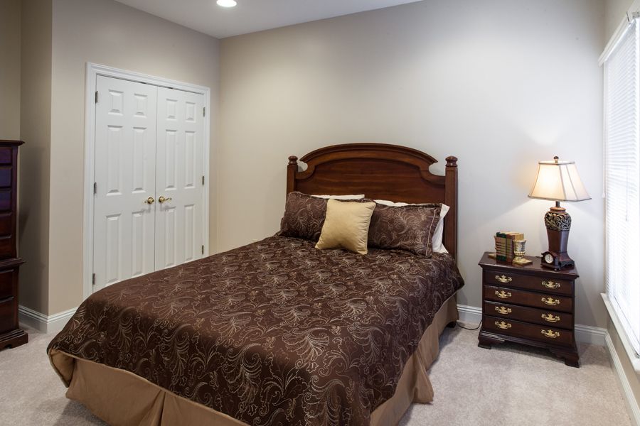 A cozy bedroom with a wooden bed frame, brown bedding, and a nightstand with a lamp.