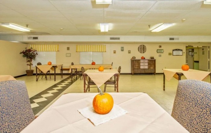 A community dining room with tables set for autumn, each featuring a small pumpkin centerpiece.