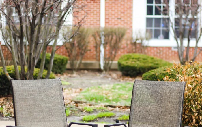 Two chairs facing a brick building with shrubs and a window in the background.