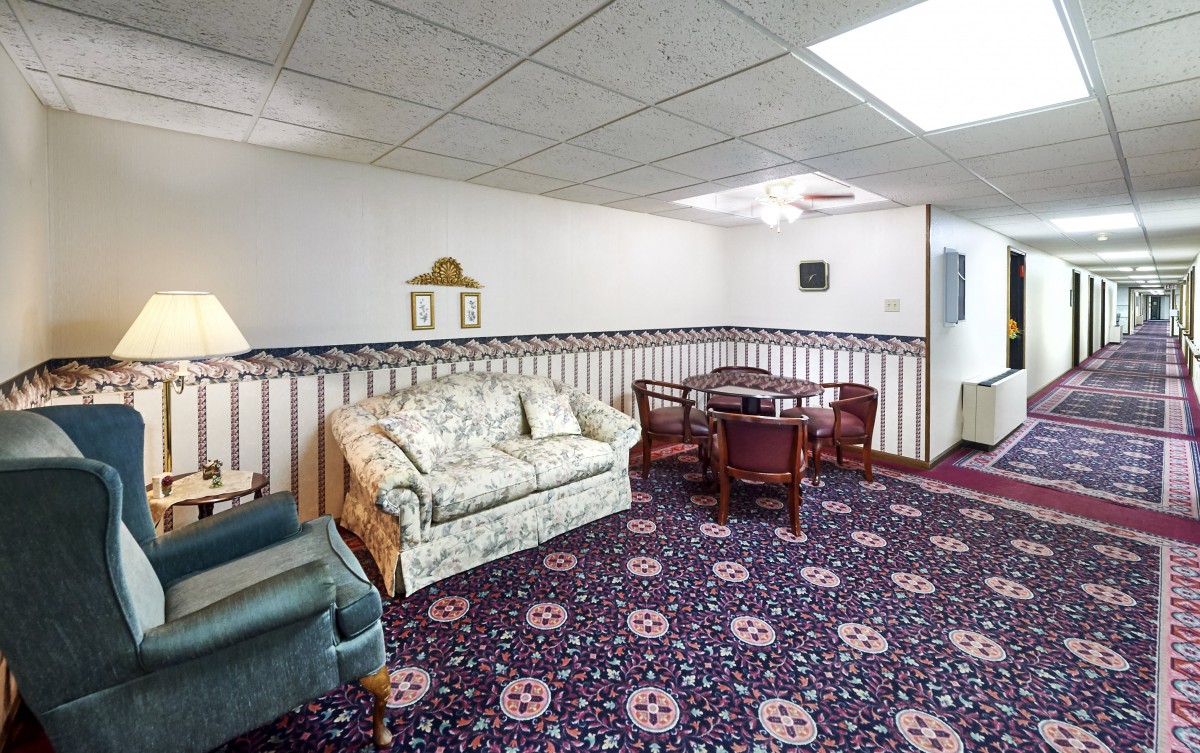 A vintage-style living room featuring a floral sofa, wooden table with chairs, and patterned carpet.